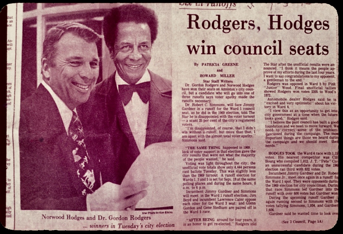 Newspaper clipping with the headline “Rodgers, Hodges win council seats” and a photograph of Norwood Hodges and a smiling Dr. Rodgers in a bow tie.